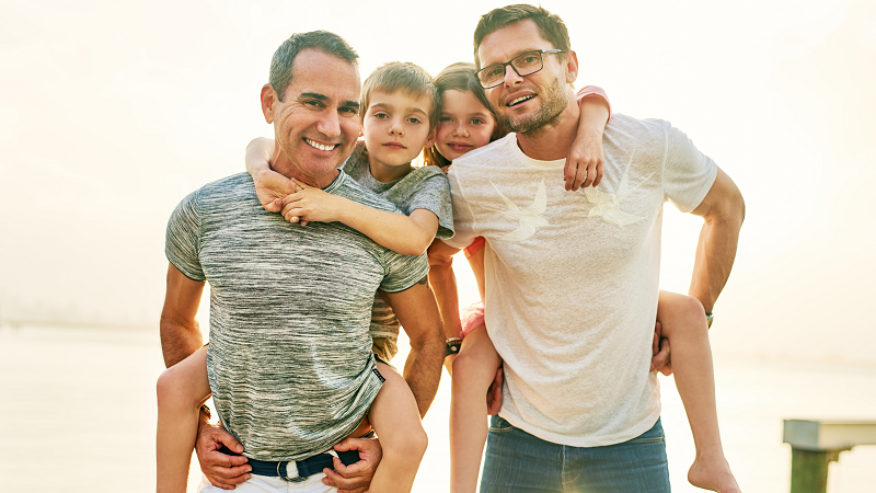 Two fathers giving piggyback rides to their children outdoors