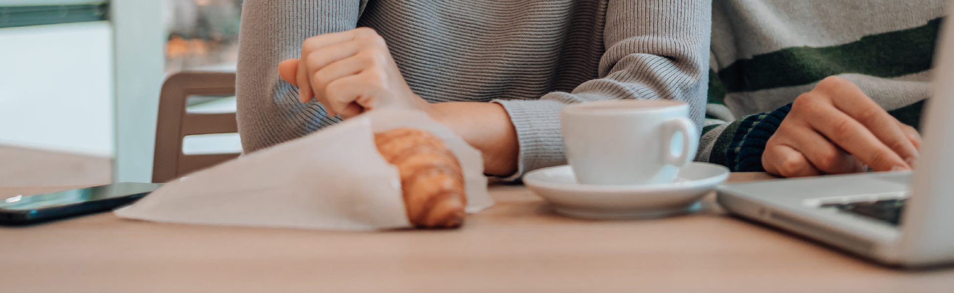 Closeup of desk with computer, phone, coffee cup and pastry