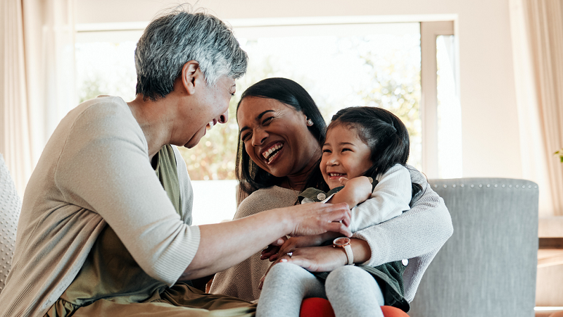 Grandmother playing with granddaughter sitting in her mother's knee